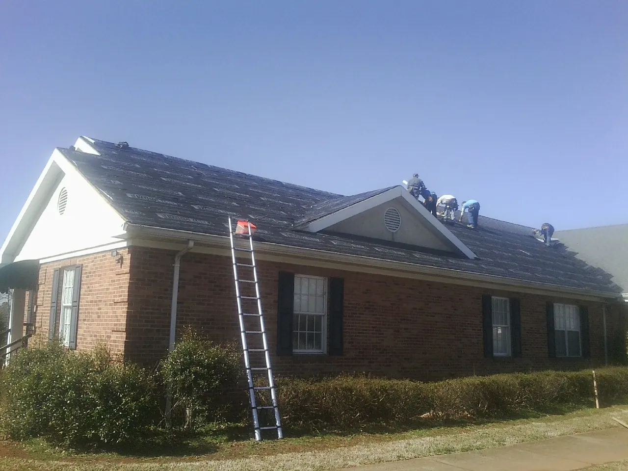 Crew tearing shingles off a brick ranch roof with a ladder set — Metal Roof Repair work by our crew in Westminster