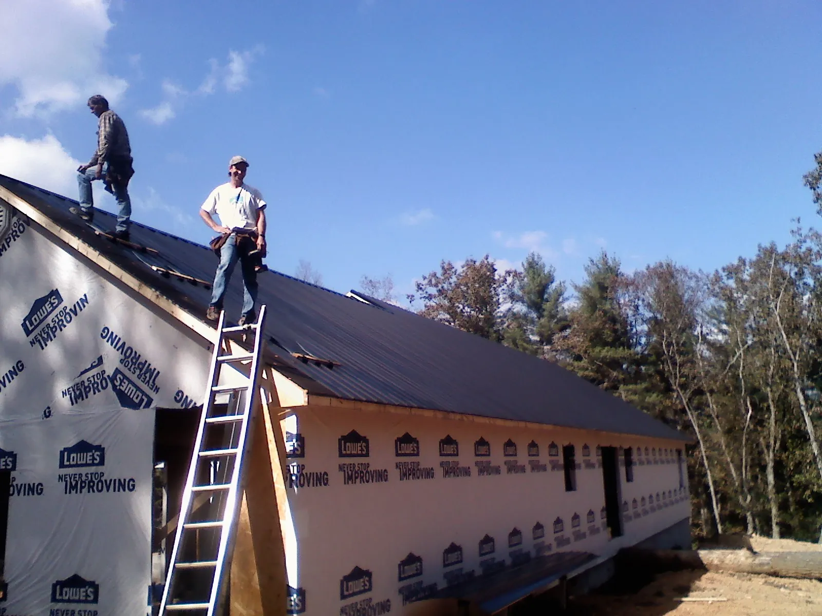 Two roofers standing on a long dark metal roof over a wrapped building in Westminster