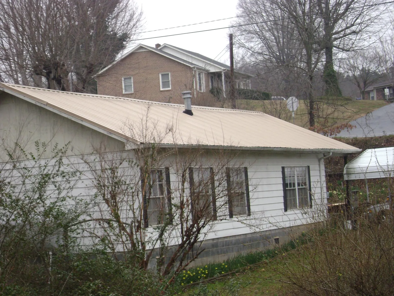 Tan metal roof on a white sided house set into a hillside — Commercial Roofing by Roofing Brothers in Westminster